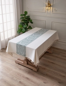 Detail of sage green floral lace pattern and woven tassels on a cream rectangle tablecloth