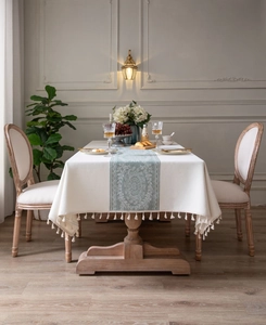 Detail of cream rectangular tablecloth featuring sage green patterns and beige tassels
