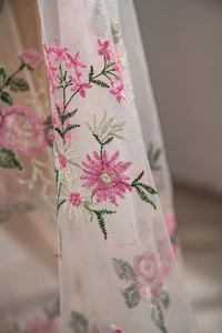 Detailed macro view of delicate pink floral embroidery on white sheer mesh fabric texture