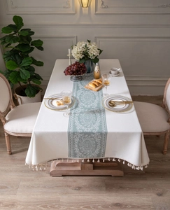Close-up of cream tablecloth with vintage green floral print and white fringe tassels
