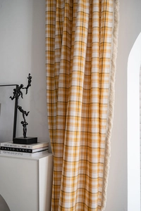 Detail view of yellow plaid curtain featuring delicate fringe edges and linen texture