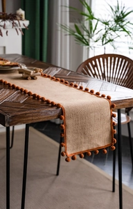 Close-up of natural jute table runner with vibrant orange pom pom fringe on a wood table