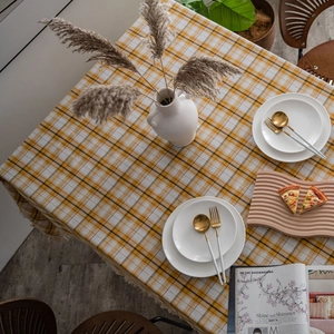 Yellow and white checkered tablecloth with fringe tassels on a dining table setup