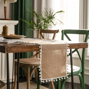 Natural burlap table runner with white pom-pom trim displayed on dark wooden table