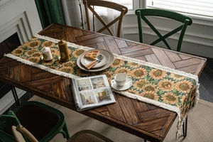 Detailed close-up of woven sunflower table runner with cream tassels on a wooden table