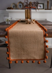 Close-up of natural jute table runner with bright orange pom-pom fringe details