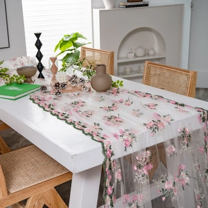 Lace table runner with pink flower embroidery and green scalloped edges on wooden table