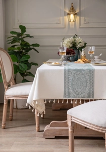 Close-up of sage green floral jacquard fabric with elegant white tassels on a cream tablecloth