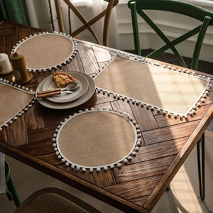 Natural jute table runner set with white pom-pom fringe on a dark wood table