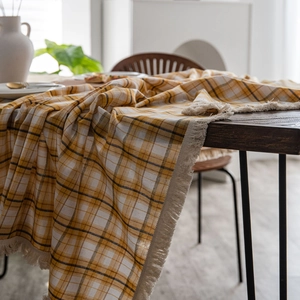 Classic yellow and white checkered tablecloth with fringe tassels on dark wood table