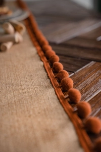 Detail of natural burlap table runner featuring rusty orange pom-poms on rustic wood