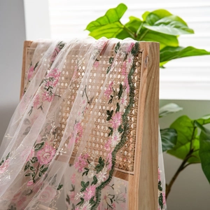 Pink floral embroidery on transparent mesh lace tablecloth draped over a rattan chair