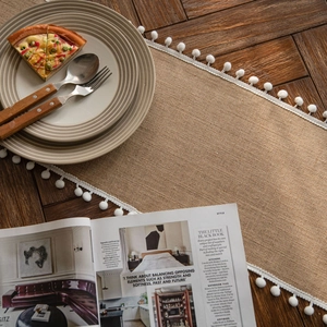 Natural jute table runner with white pom-pom trim on a rustic wooden dining table