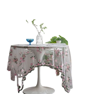 Wit kanten tafelkleed met roze bloemenborduursel op een ronde tafel als decor
