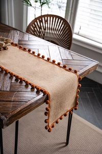 Close-up of rustic natural jute table runner with bright orange pom-poms on a wooden table