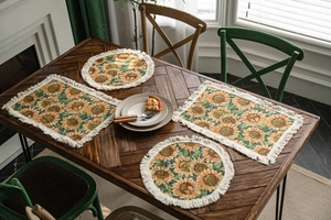 Detail of sunflower placemats with cream tassels on a dark wood table decor