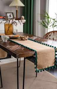 Détail du chemin de table en jute naturelle avec franges à pompons verts sur bois