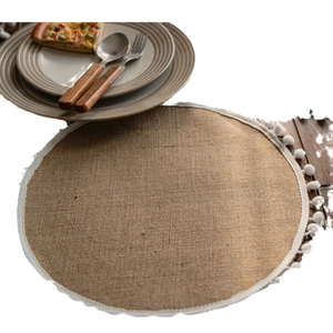 Natural jute woven table runner with white pom-pom fringe in a cozy dining setting