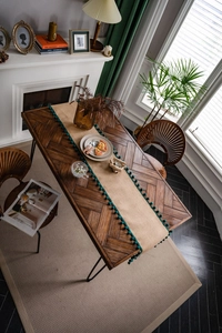 Détail du chemin de table en jute beige avec pompons vert foncé sur une table en bois