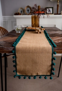 Gros plan d'un chemin de table en jute naturelle avec des bordures de pompons vert foncé
