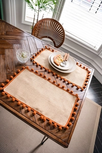 Detail of natural jute placemats with bright orange pom-poms on a wooden table