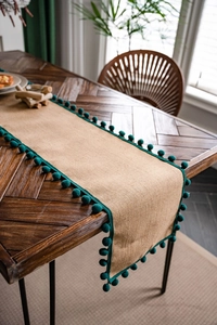 Détail de chemin de table en jute naturelle avec pompons vert forêt sur table en bois