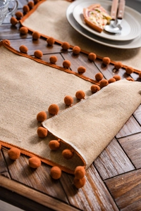 Close-up of natural burlap table runner with orange pom-poms on dark wooden table
