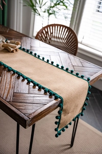 Gros plan sur un chemin de table en jute naturelle avec bordure à pompons vert foncé