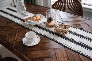 Detalle de camino de mesa tejido en blanco y negro con diseño zigzag sobre mesa de madera