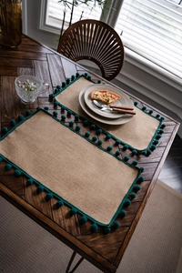Détail de sets de table rectangulaires en jute naturelle avec pompons vert foncé sur bois