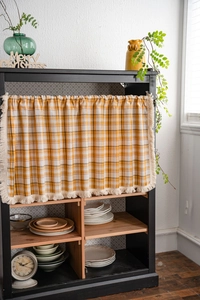 Detail showing yellow gingham cotton fabric and beige tassel fringe on the cabinet curtain
