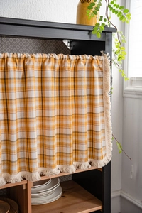 Detailed view of yellow plaid kitchen curtain with delicate tassel edges and cotton texture