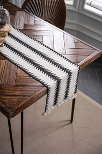 Detalle de camino de mesa tejido a mano con patrones geométricos negros y flecos