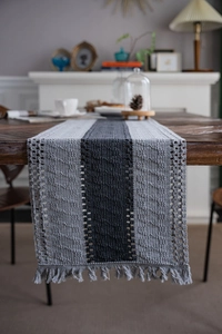 Detailed knit texture and tassels of a grey striped table runner on a wooden dining table