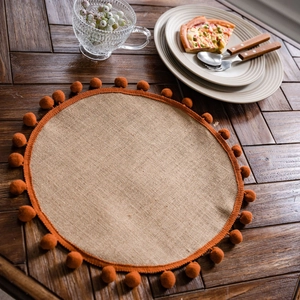 Natural jute woven placemat with orange pom-poms on a dark wood dining table