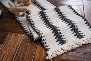 Detalle de camino de mesa tejido con patrones negros y borlas de algodón decorativas