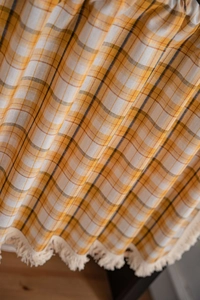 Detail of orange plaid curtain fabric with decorative cream tassels on wooden background