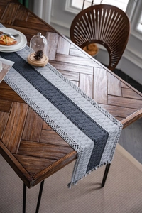Close-up of gray woven table runner with striped stitching, hollow lace, and tassels