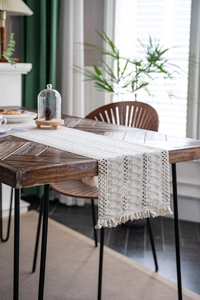 Detail of bohemian cream woven table runner with intricate hollow crochet and tassels