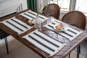 Detalle de cuatro manteles boho con patrones geométricos negros y flecos