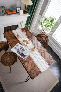 Detail of wooden dining table with herringbone pattern and white woven table runner