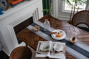 Detail of gray woven table runner with tricolor stripes and tassels on wooden table