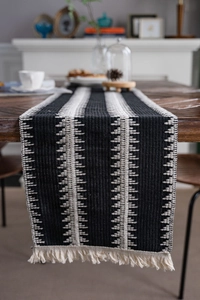 Détail du chemin de table en coton à rayures noir et blanc avec franges sur table en bois