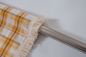 Detailed close-up of orange plaid fabric kitchen curtain with fringe on a metal rod
