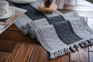 Close-up of grey knitted table runner featuring woven stripes and textured fringe detail
