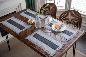 Close-up of grey striped woven table mats with fringe on a wooden dining table