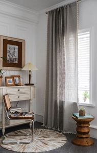 Detailed close-up of grey linen curtain featuring elegant white tassel trim and embroidery