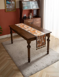 Detailed texture of orange jacquard table runner with large floral patterns and beaded tassels