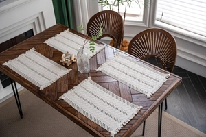 Close-up of four woven cream cotton placemats with dark wave patterns and fringe on a wood table