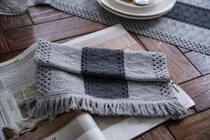 Detail of grey knitted table runner showing striped textures and fringe on a wooden table